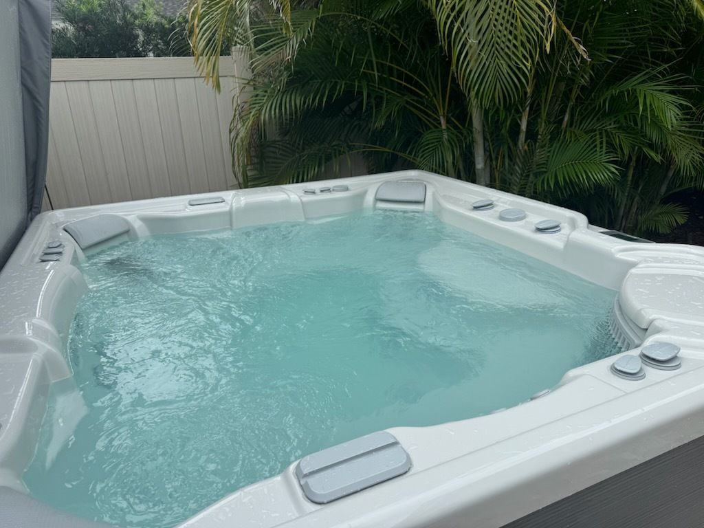 Backyard hot tub with clear water, white shell, and tropical plants behind it