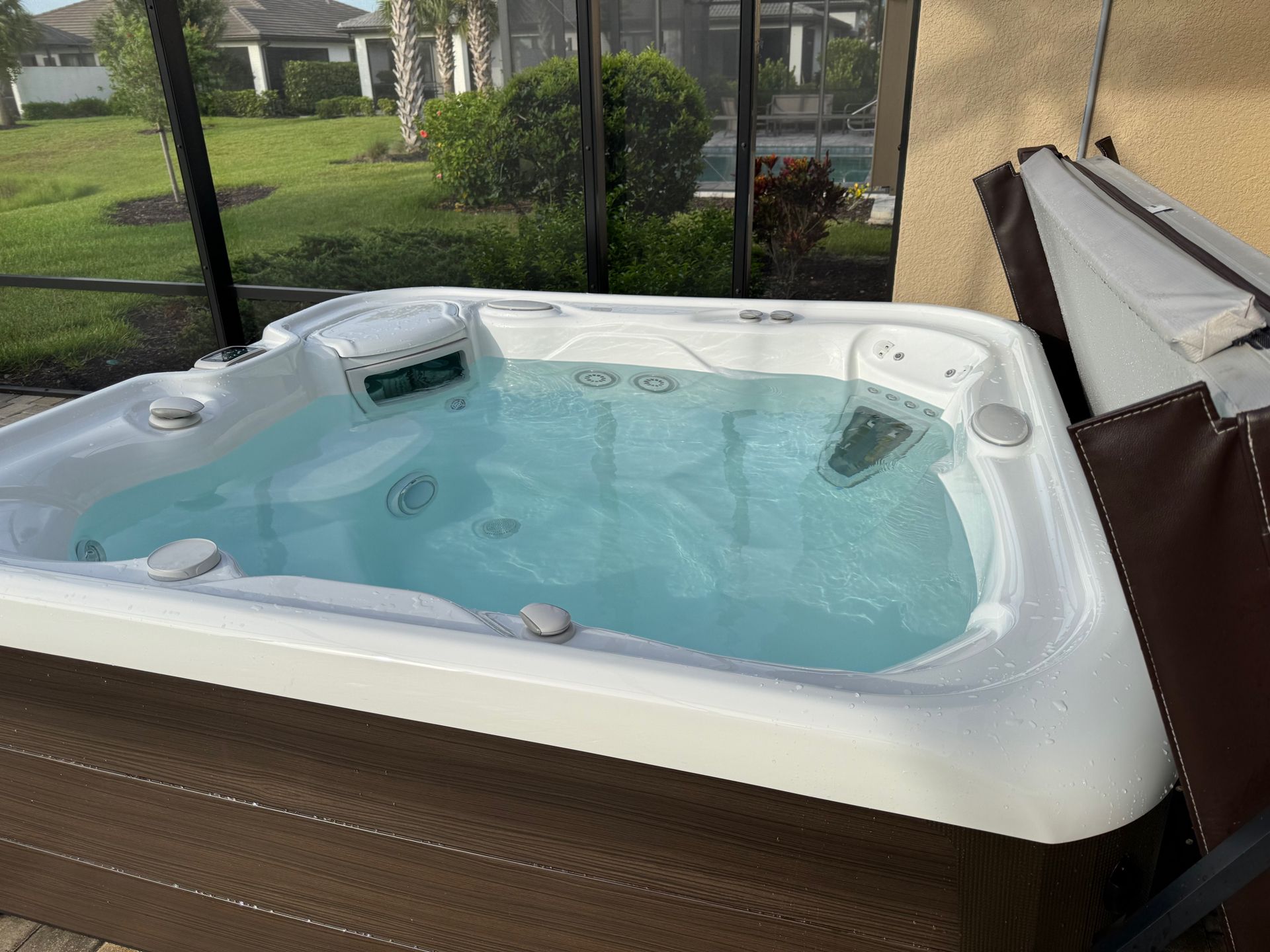 Hot tub with clear water, outdoors on a patio, partially covered with its folded brown cover.