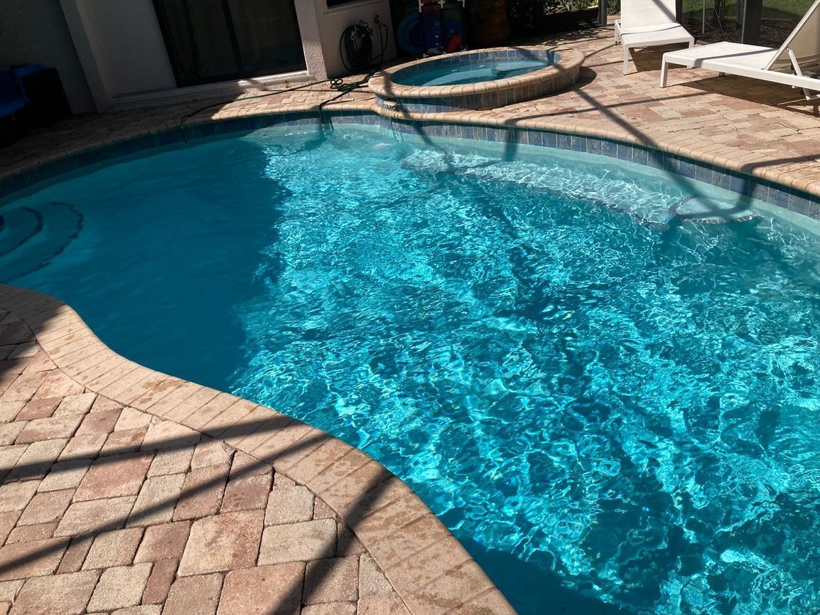 Pool with clear blue water and a circular hot tub. Brick patio surrounds the pool.