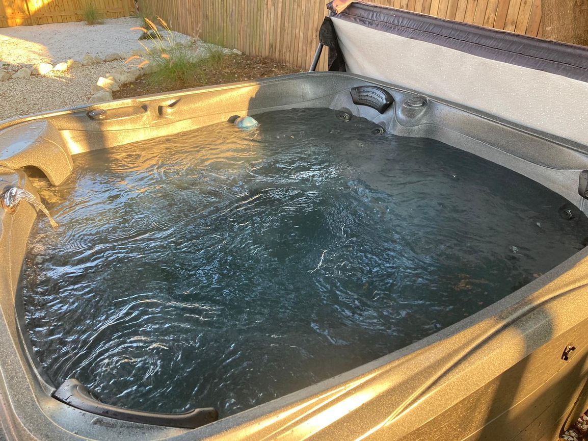 Hot tub filled with bubbly water, outdoors. Beige tub with partly open brown cover.
