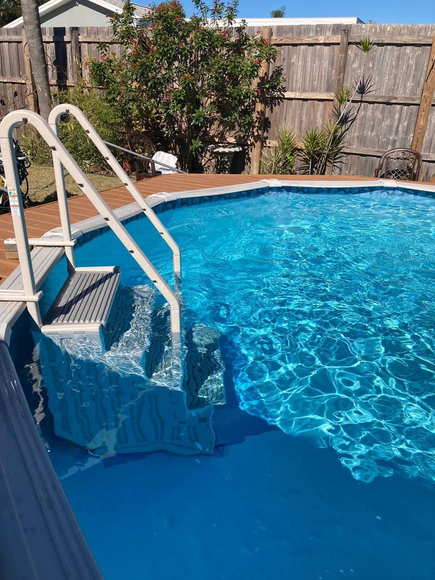 Above-ground swimming pool with blue water and white ladder steps against a wooden fence.