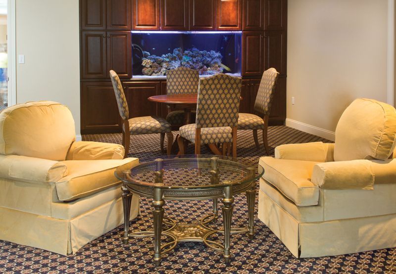 Living room with two cream armchairs, a glass-topped table, and a dining set in front of an aquarium.