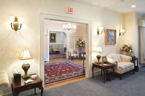 Interior of a formal, well-lit room with a doorway to another room. Includes furniture and an exit sign.