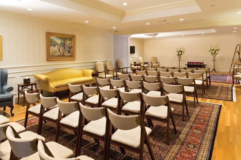 A meeting room with rows of chairs, a yellow sofa, and a rug.