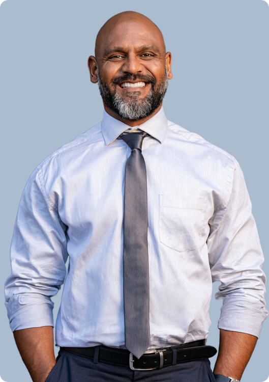 A smiling person wearing a light blue dress shirt, grey tie, and dark trousers against a light blue background.