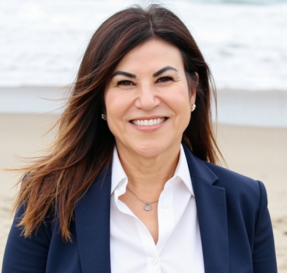 Smiling woman in a navy blazer and white shirt standing outdoors near the beach