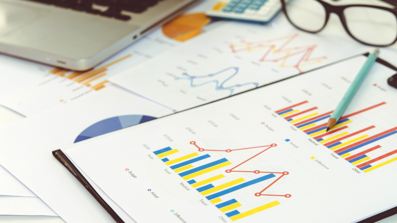 Notebook with colorful charts and graphs beside glasses, a laptop, and a pencil on a desk