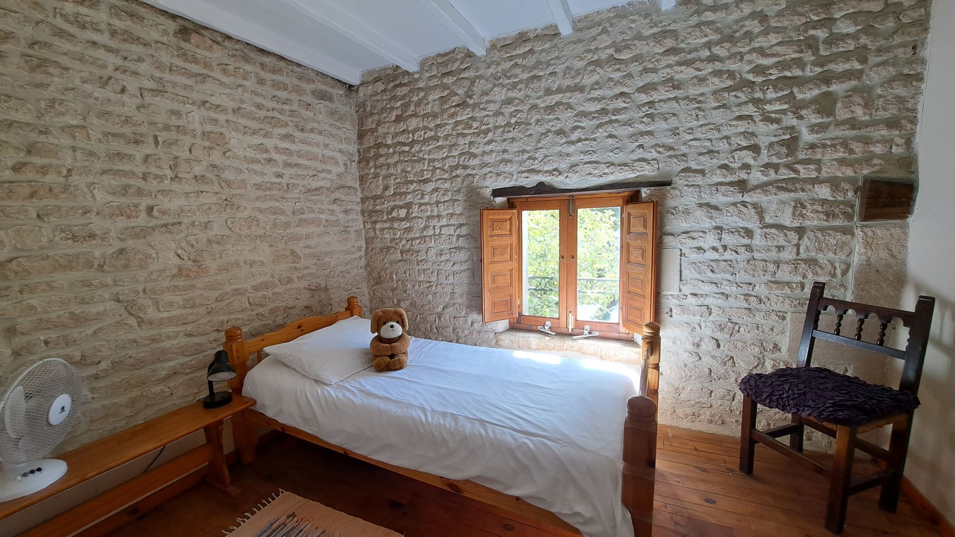childrens single bed with cuddly toy in a room with a stone wall