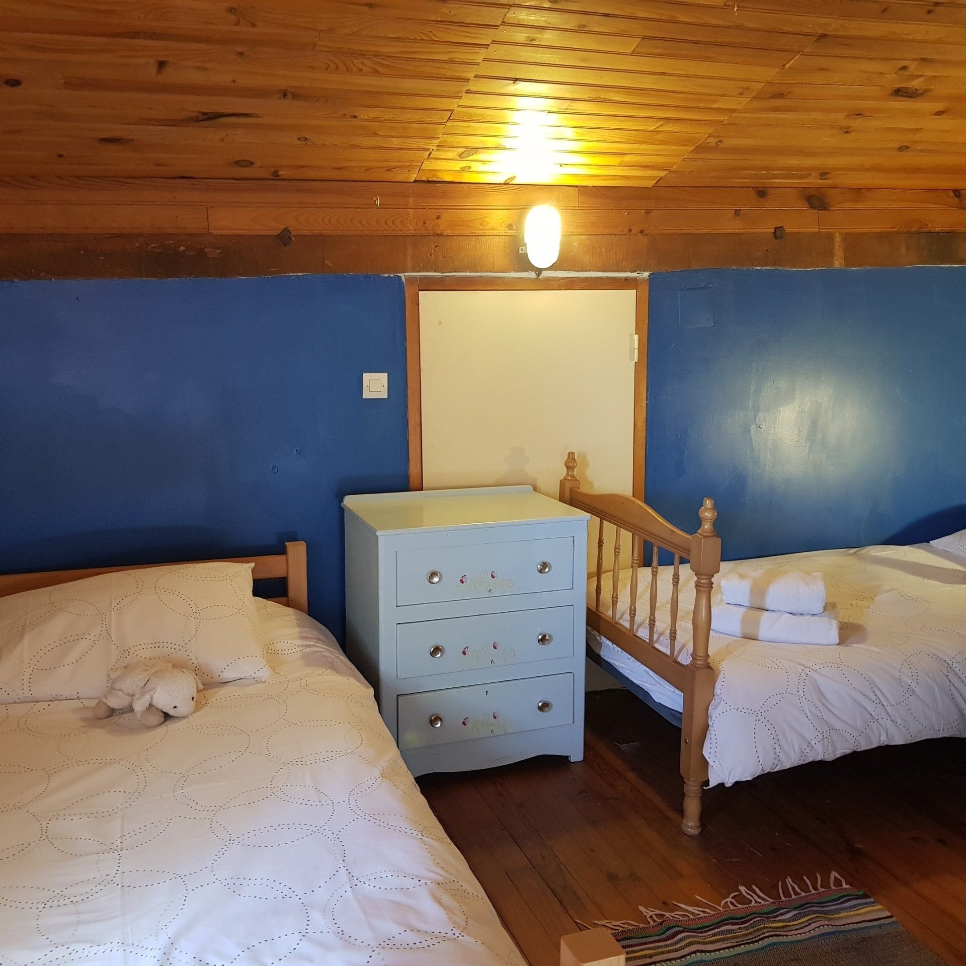 two single beds in an attic bedroom with blue walls and wooden lambris ceiling