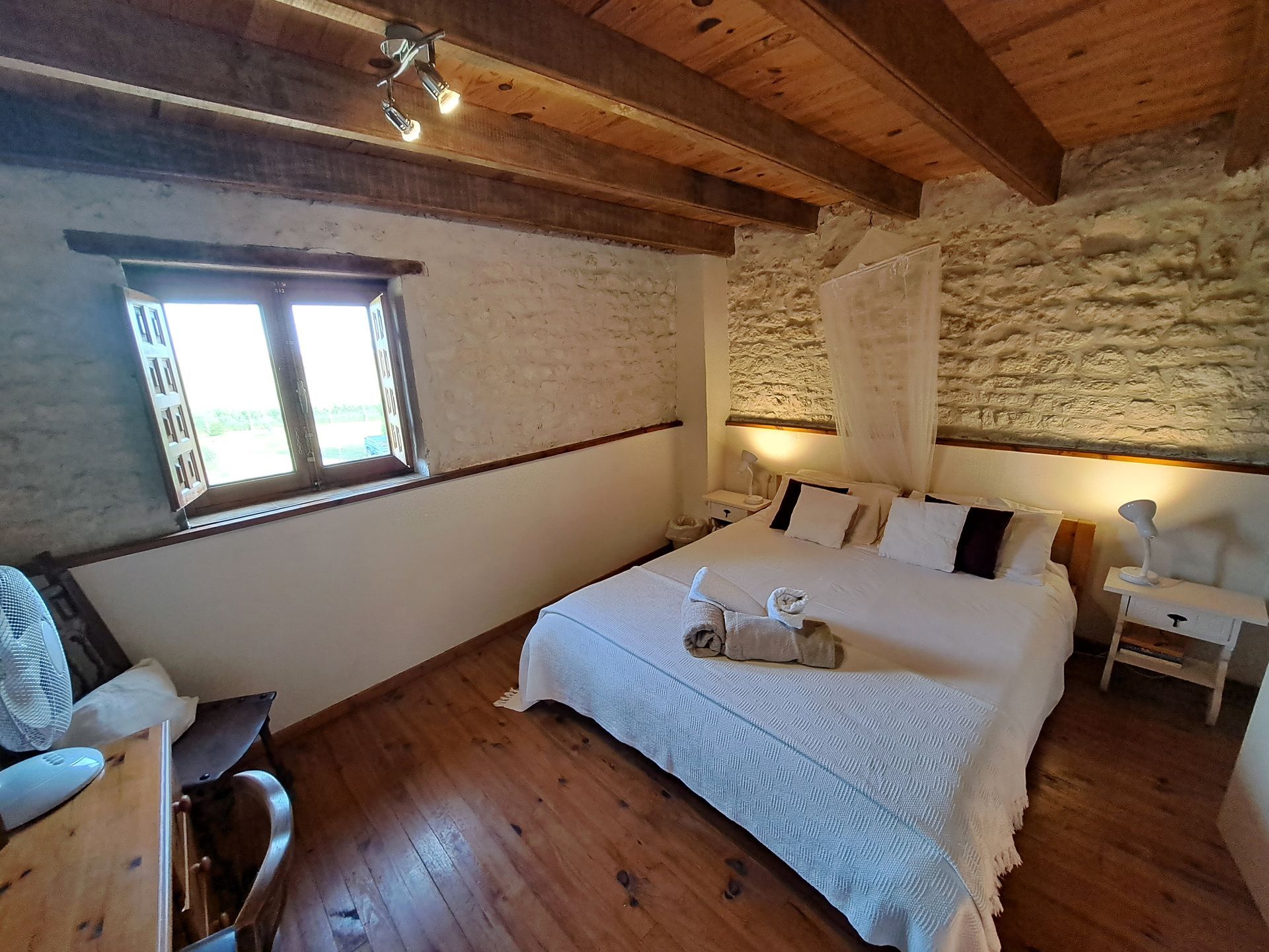 king sized bed with white bedding. exposed Stone walls uplit by side lamps