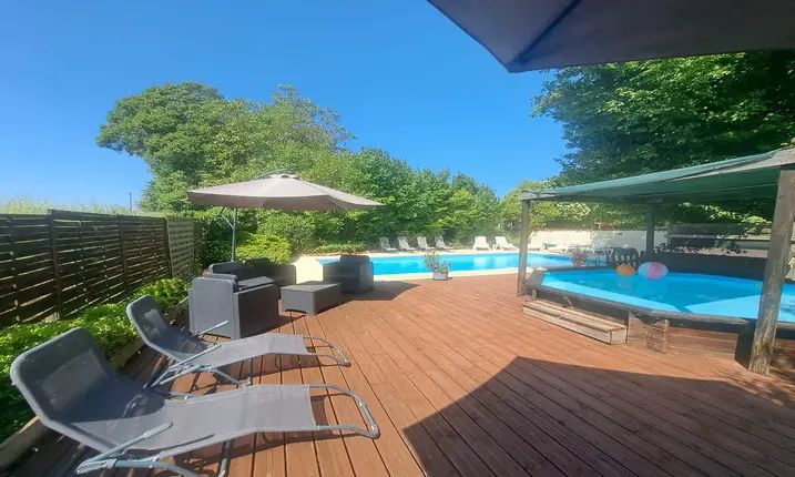 terrasse en bois pour bronzer avec transats gris et une piscine pour enfants avec une piscine plus grande en arrière-plan