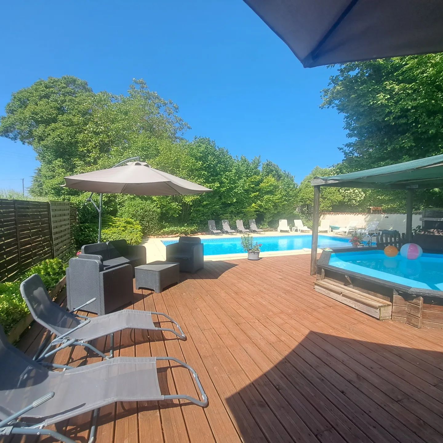 wooden sunbathing deck next to a pool with grey sunbeds