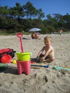 toddler sat on a beach with bucket and spade