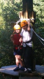 two boys with yellow helmets and safety harness  at a rope park in the trees