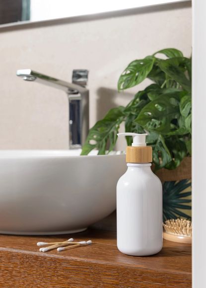 Dispensador de jabón blanco junto a un lavabo de baño con grifo cromado y planta verde.