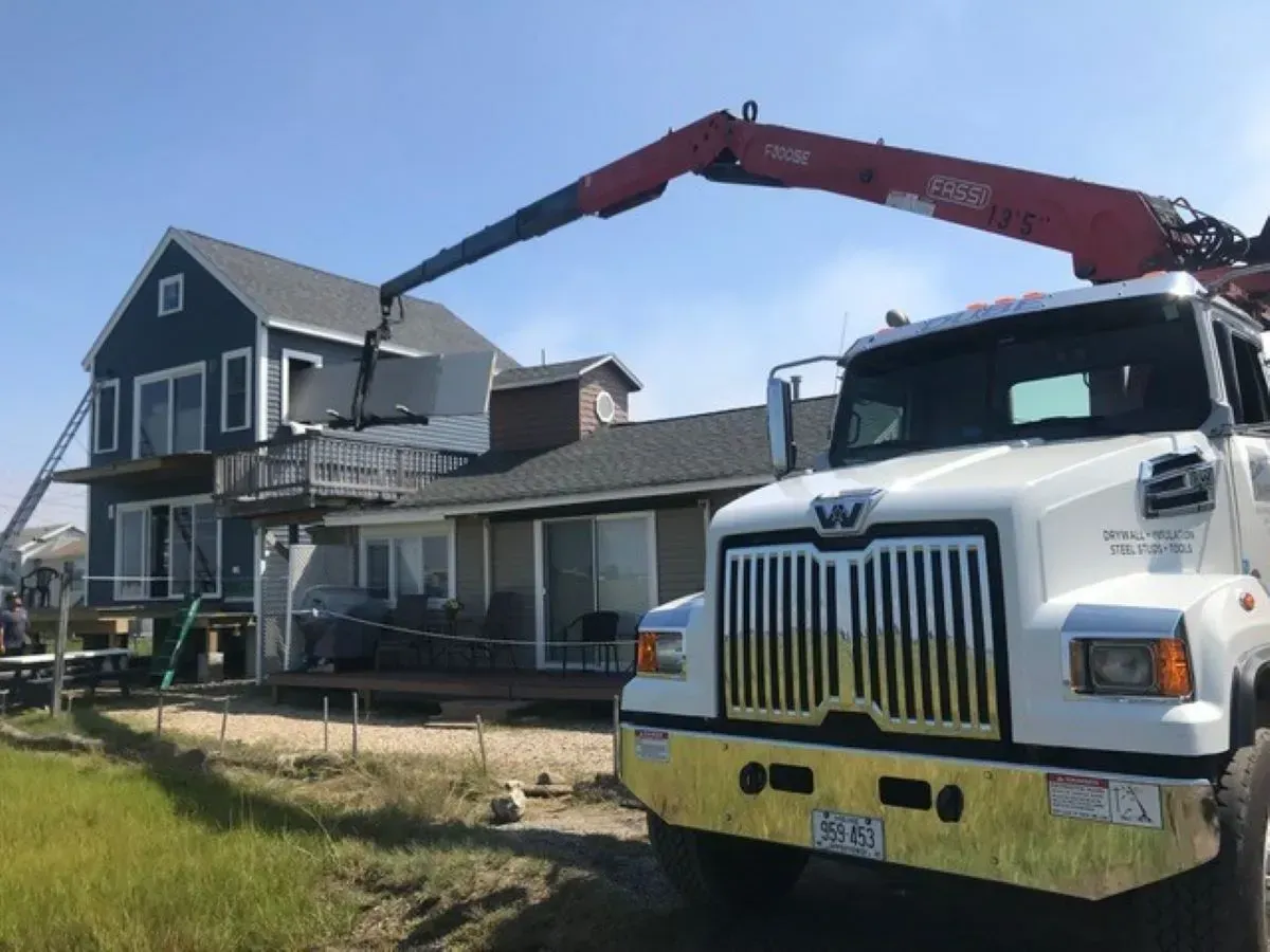A white truck with a crane attached to it is parked in front of a house.