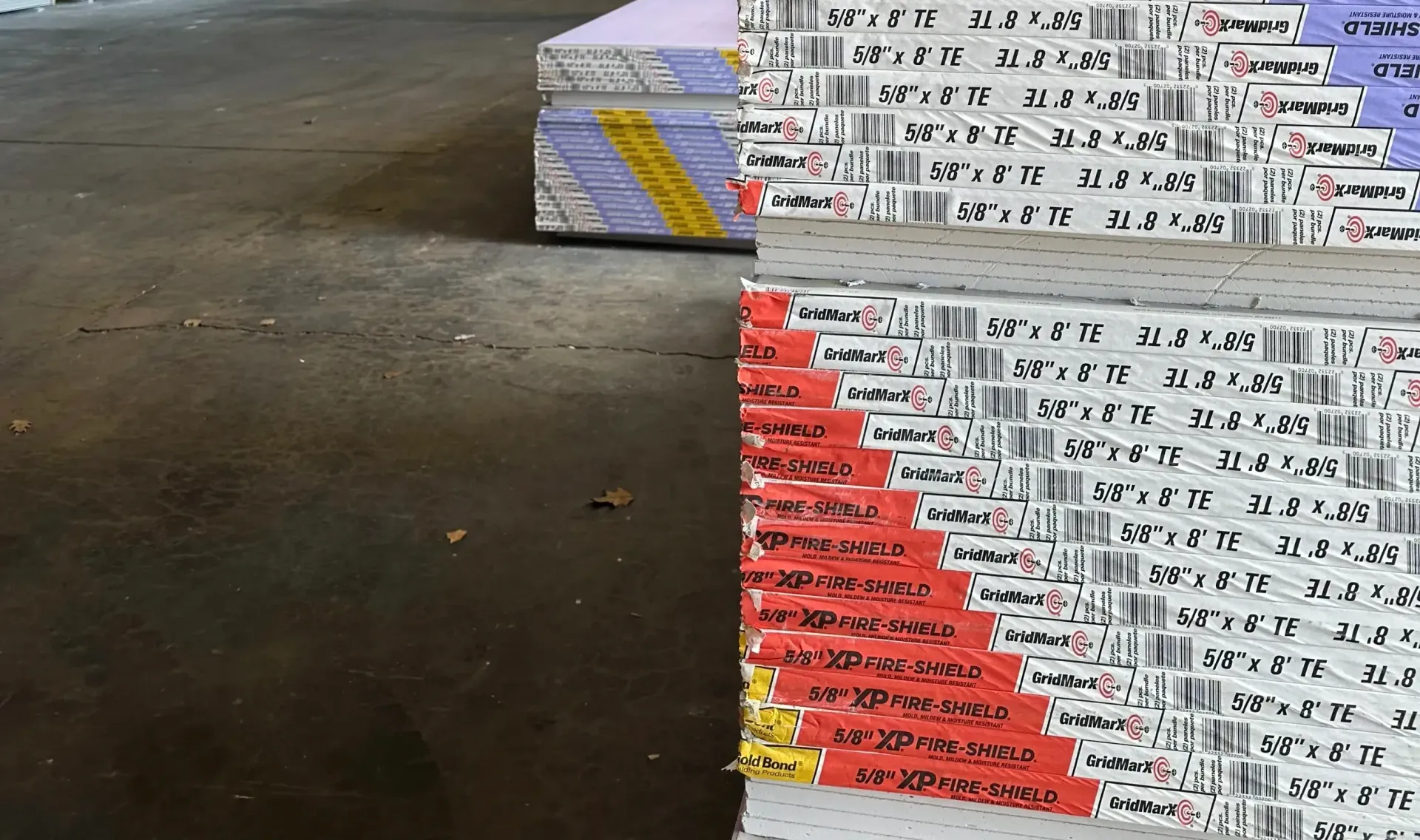 Stacks of white industrial boards with red and purple markings, arranged in a warehouse.
