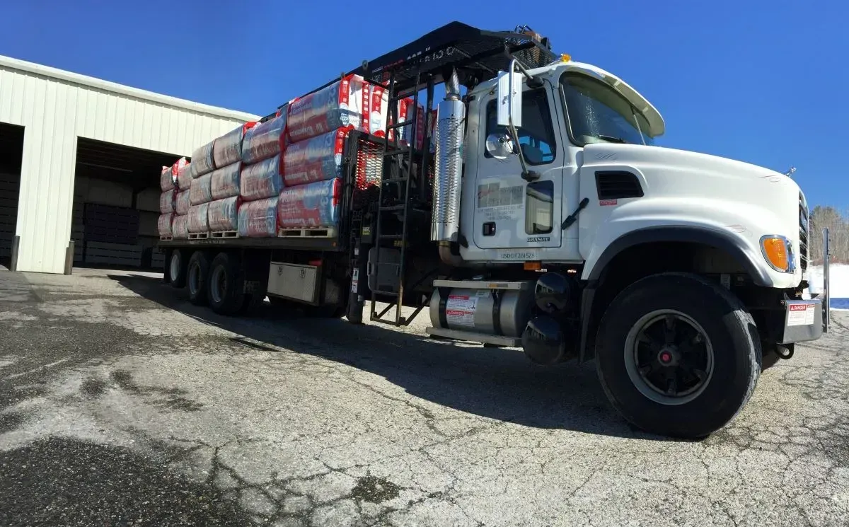 A white truck with a crane on the back is loaded with bricks.