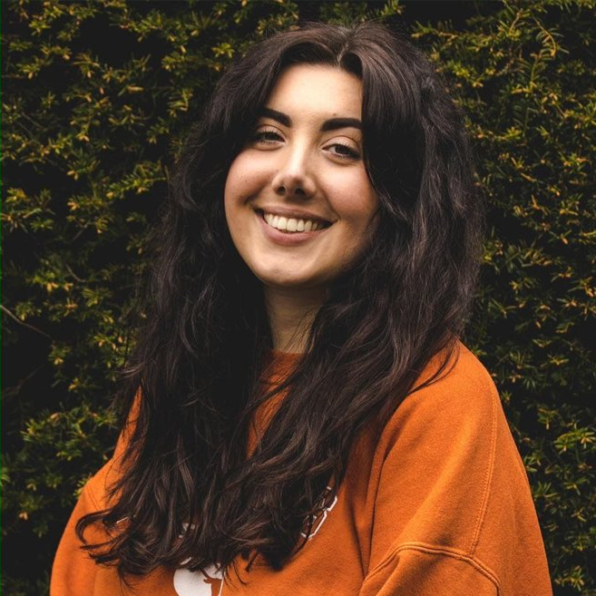 Photo of Cat, who has long dark hair and is wearing an orange top.