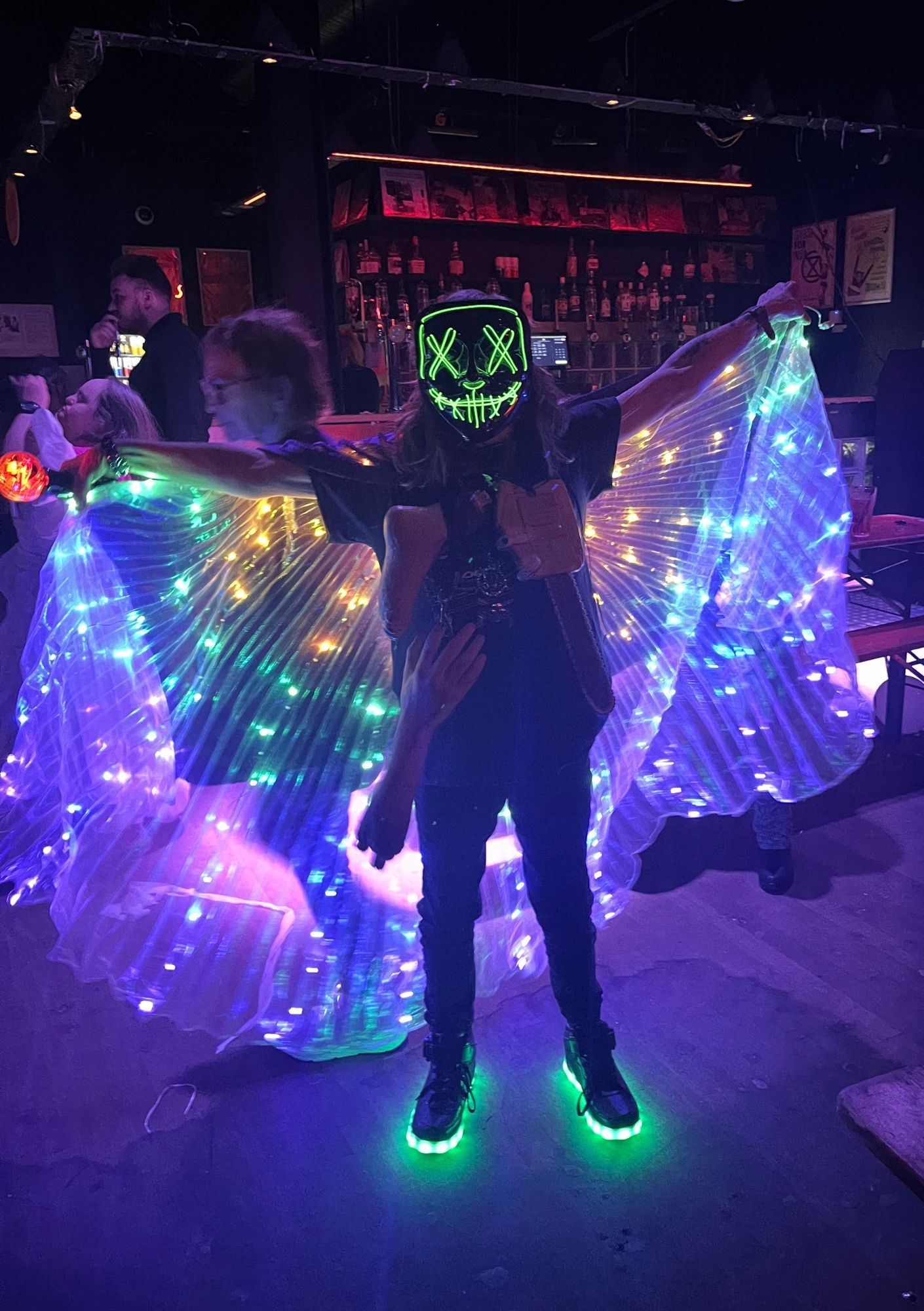 A person in a dark room wearing a mask with a neon skull face and a cape with neon lights