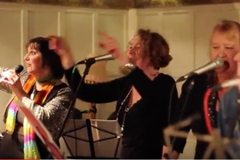 Three women singing, each person is standing in front of a microphone