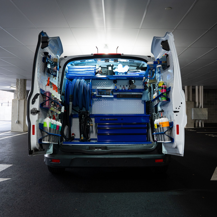 Open van in a parking garage, rear doors open with organized cleaning equipment inside.