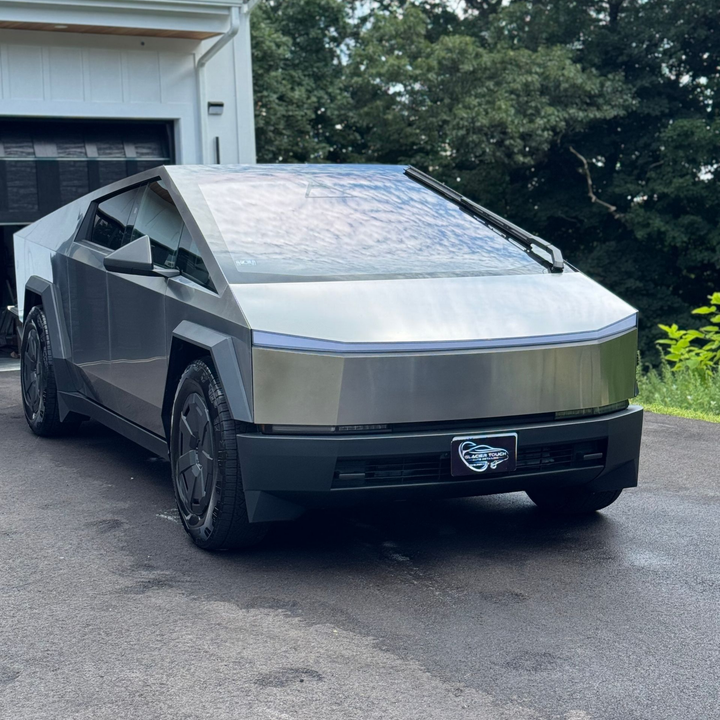 Silver Tesla Cybertruck parked in a driveway beside a garage, front view