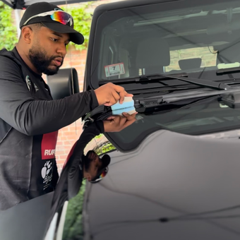 Man cleaning a black car windshield with a blue cloth outdoors