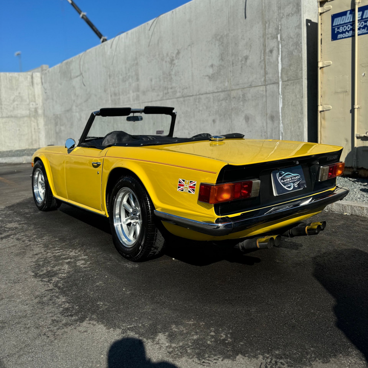Yellow vintage convertible sports car parked outdoors by a concrete wall.