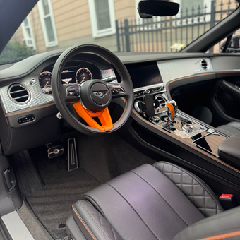 Luxury sports car interior with black leather and orange steering wheel accents.