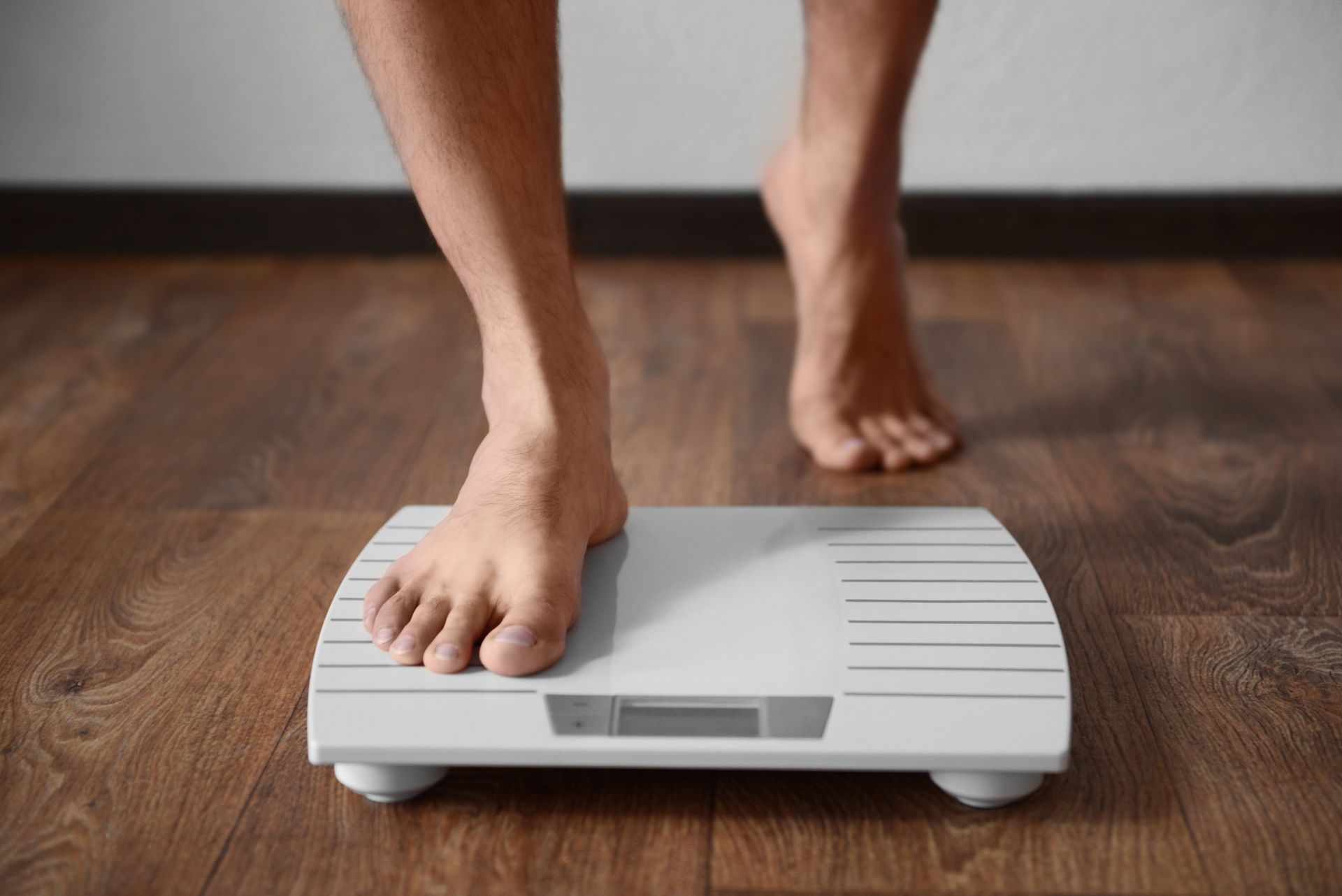 Bare feet stepping onto a white bathroom scale on a wooden floor.