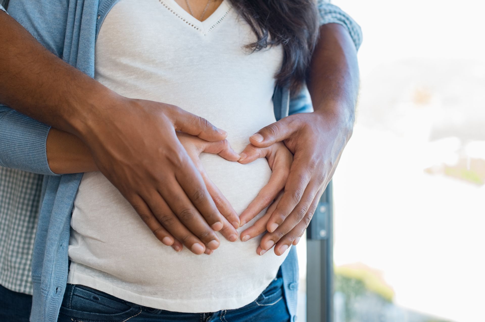 Pregnant belly with hands forming a heart shape.