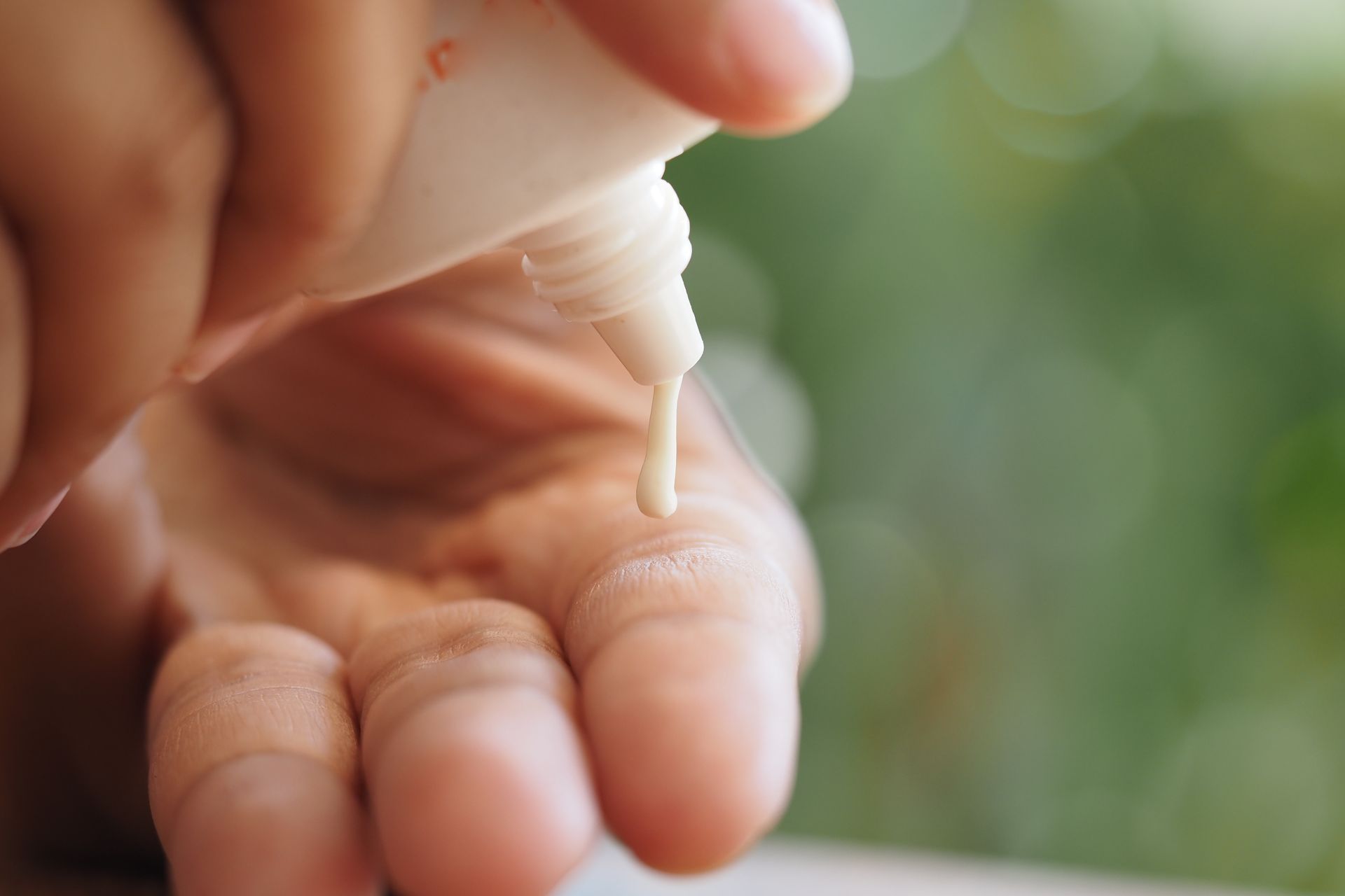 Hand dispensing lotion from a white tube onto a finger.