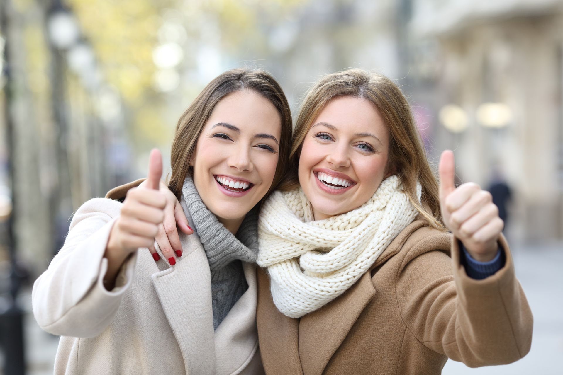 Two women, thumbs up, smiling in a city street. 
