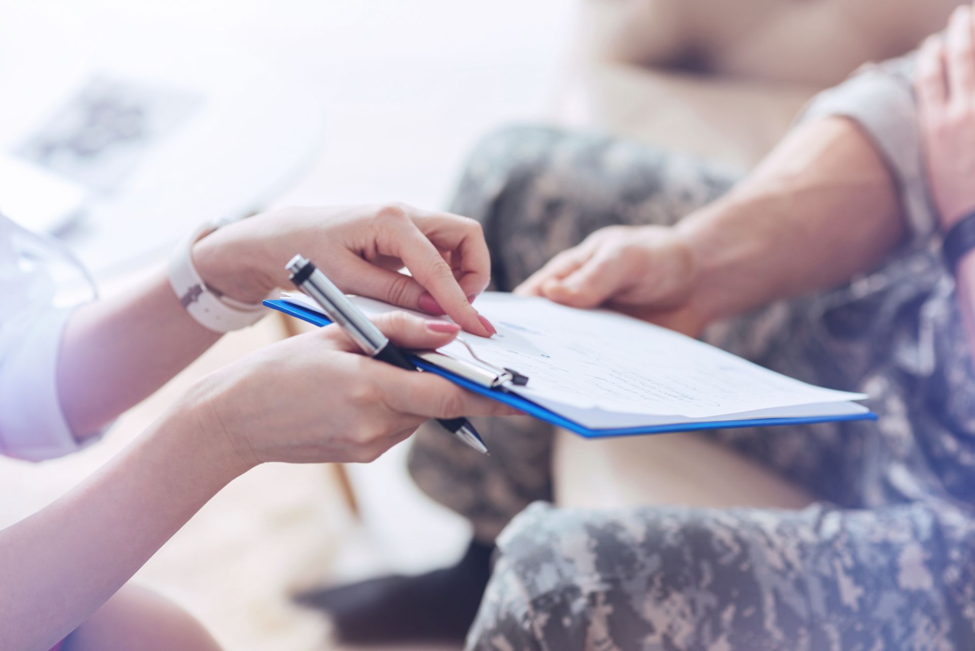 Woman points to a document on a clipboard held by a person in camouflage clothing.