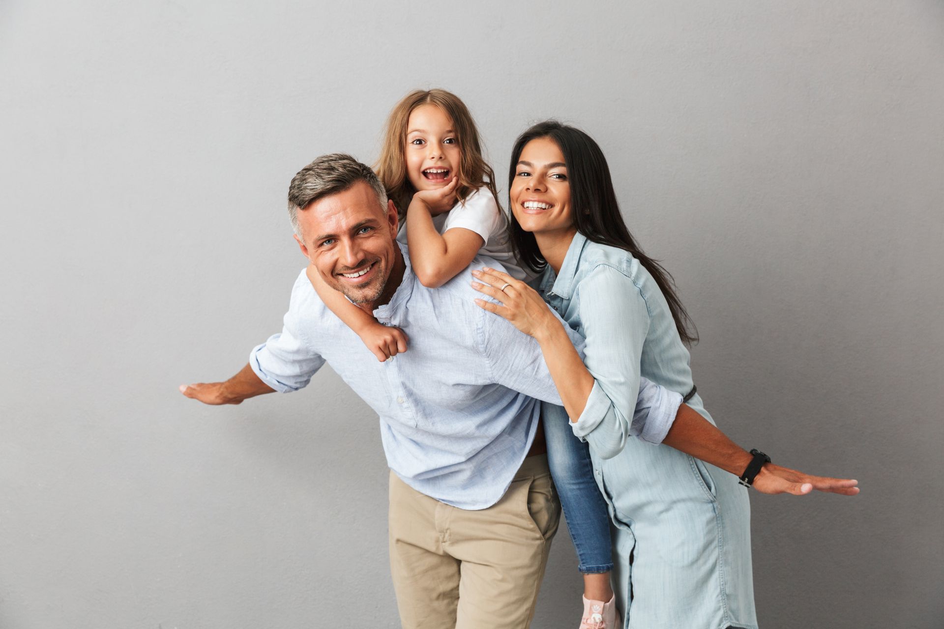 Family smiling and playfully posing together in front of a gray background.