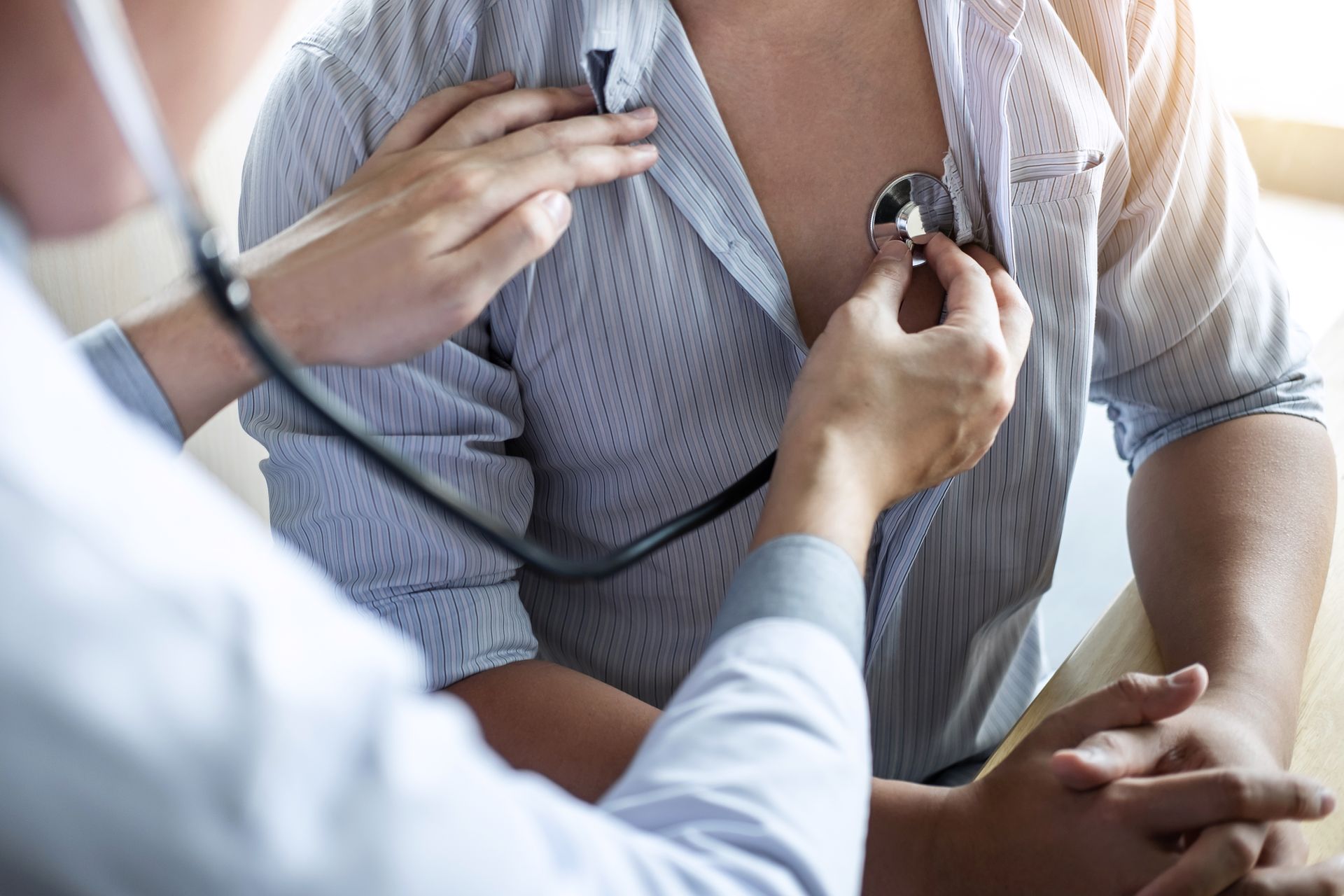 A medical professional using a stethoscope to listen to a patient's chest during a physical examination.