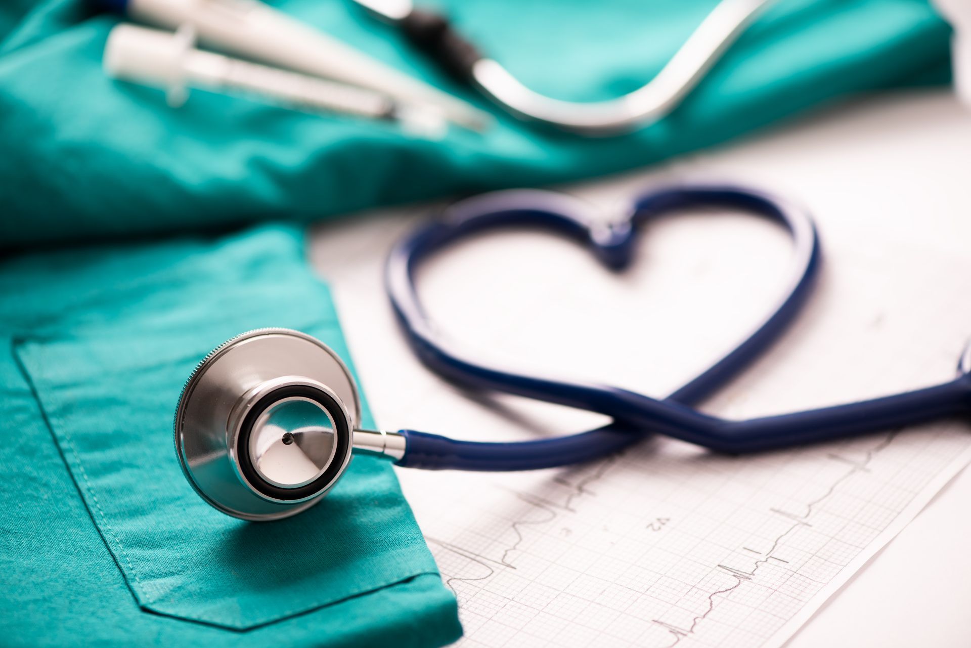 Stethoscope in heart shape on a medical chart, next to teal scrubs and syringes.
