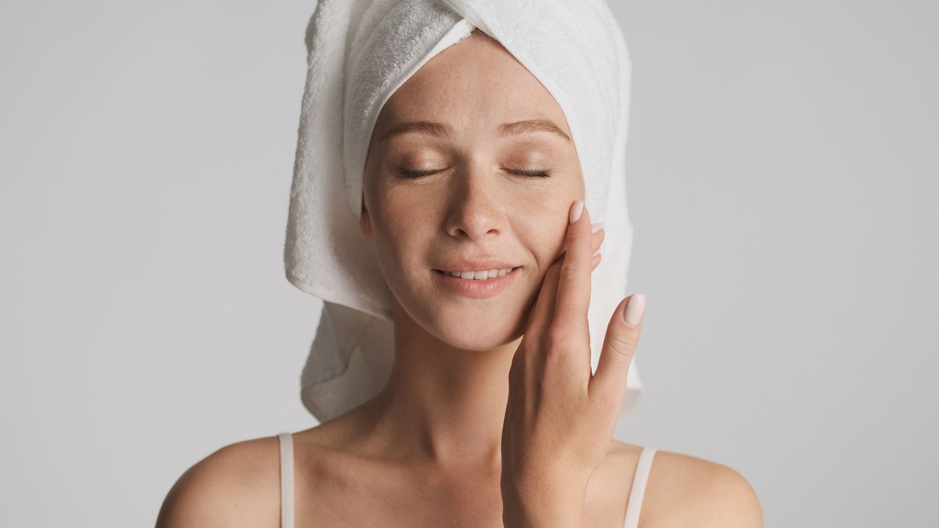 Woman with towel on head touches face, eyes closed.