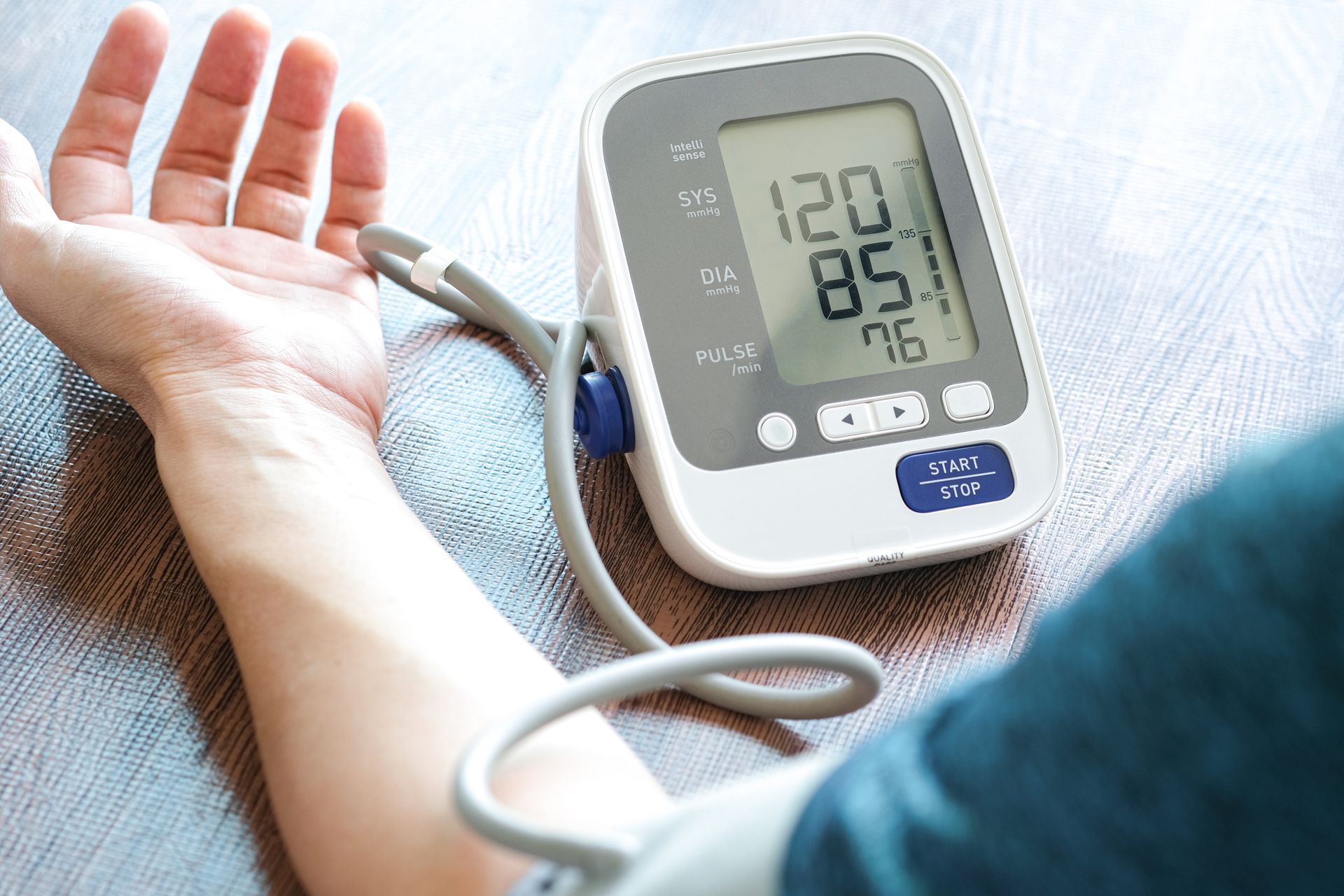 A person wearing a blood pressure cuff on their arm, with a digital monitor displaying 120/85 mmHg and a pulse of 76.