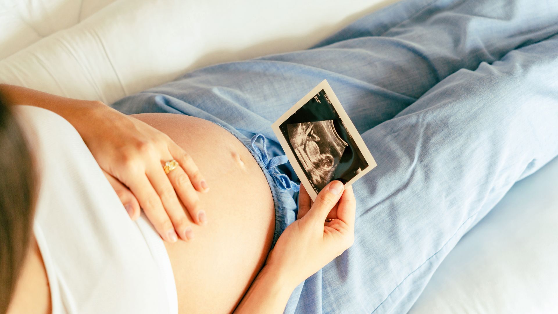 Pregnant person holding ultrasound photo, resting on belly.