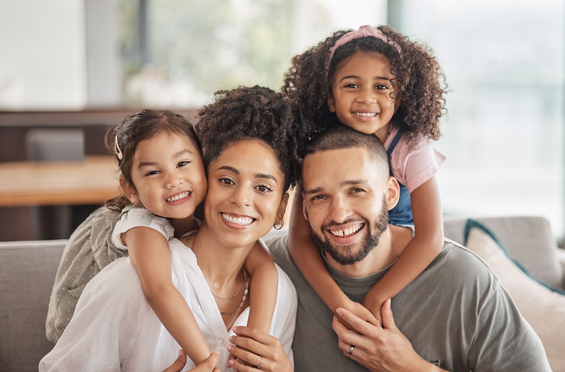Family smiling, posing together indoors. Two young girls on parents' backs.