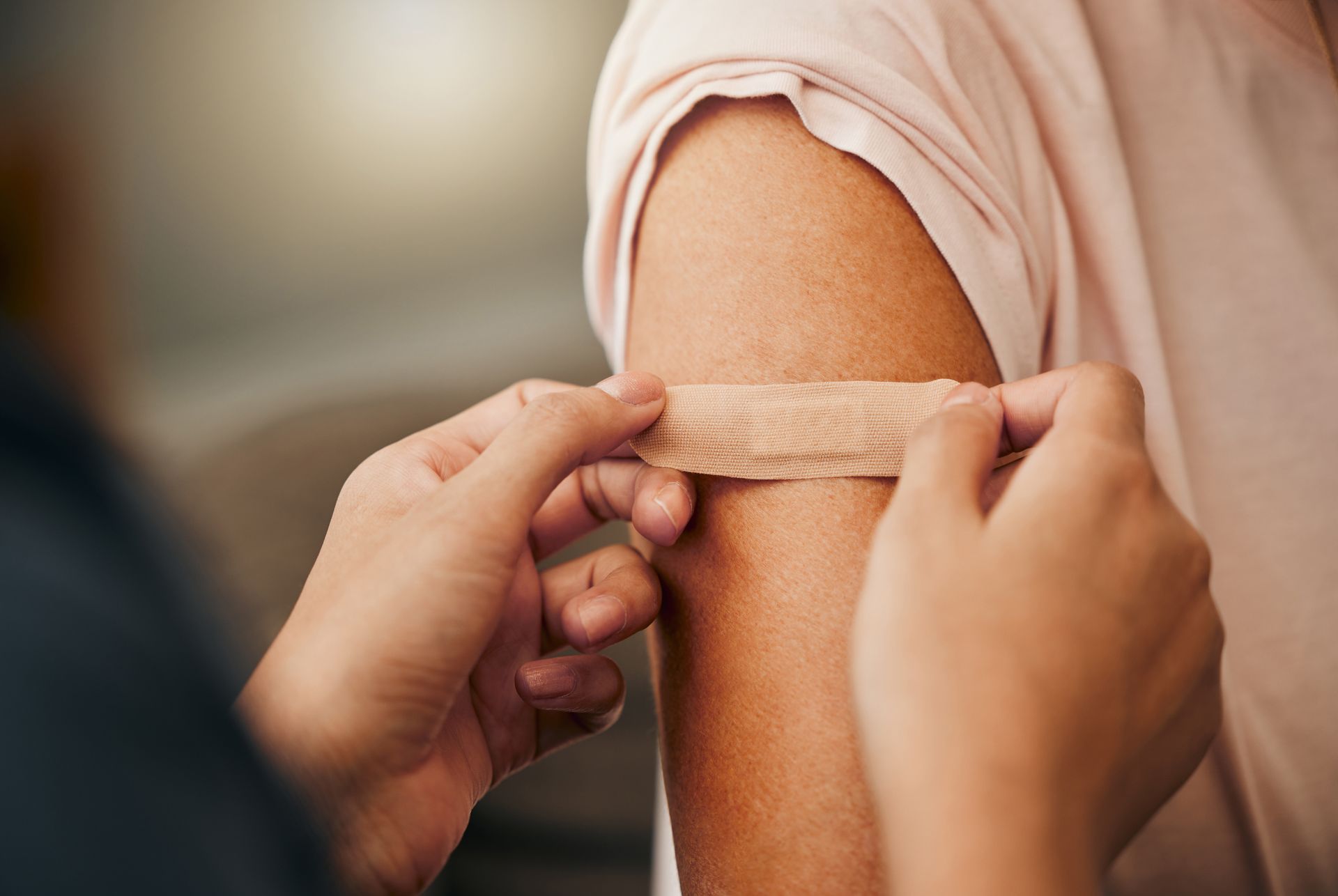 Person applying a bandage to another person's upper arm, near the injection site.