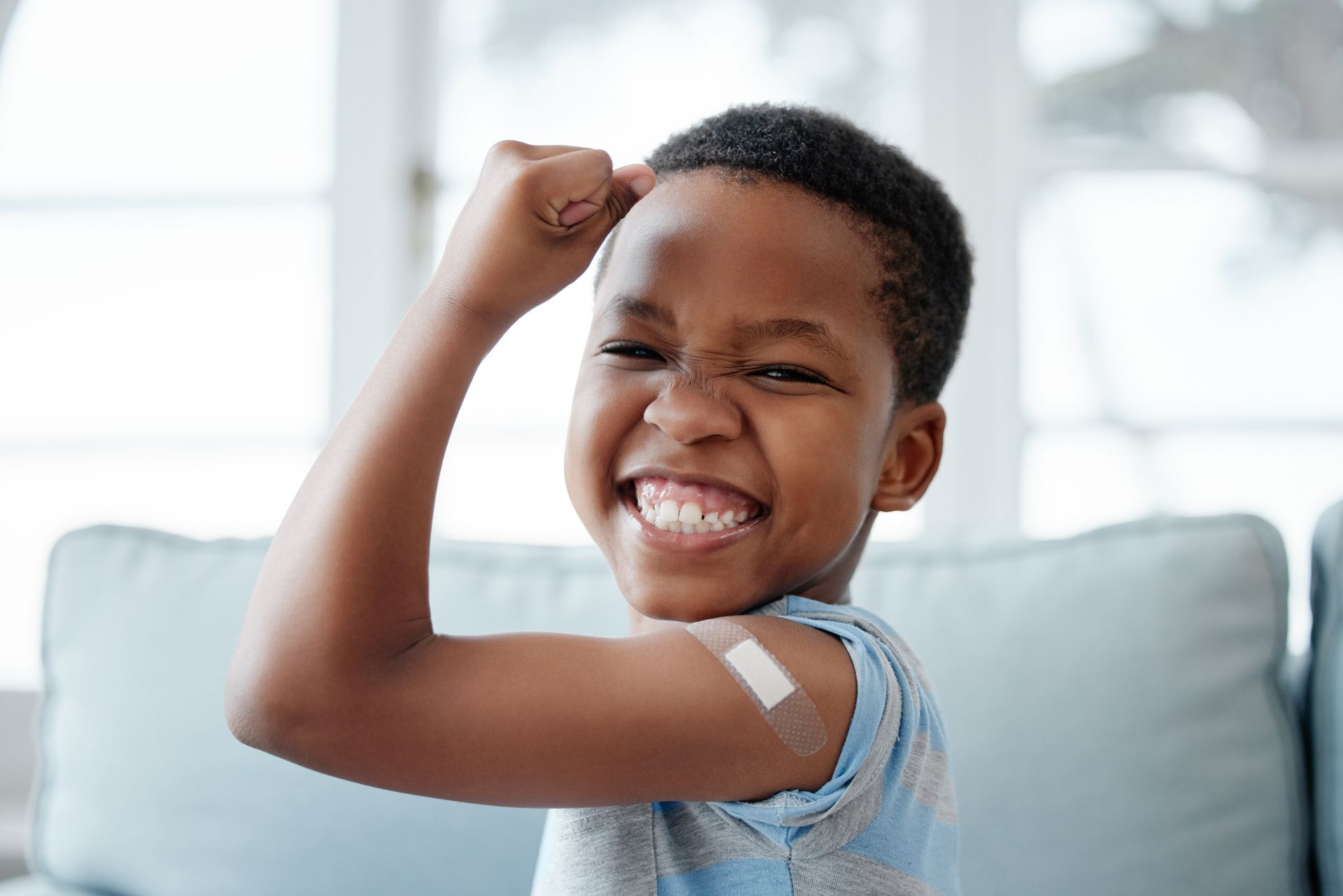 A smiling child flexing their arm to show a bandage after receiving a vaccination.