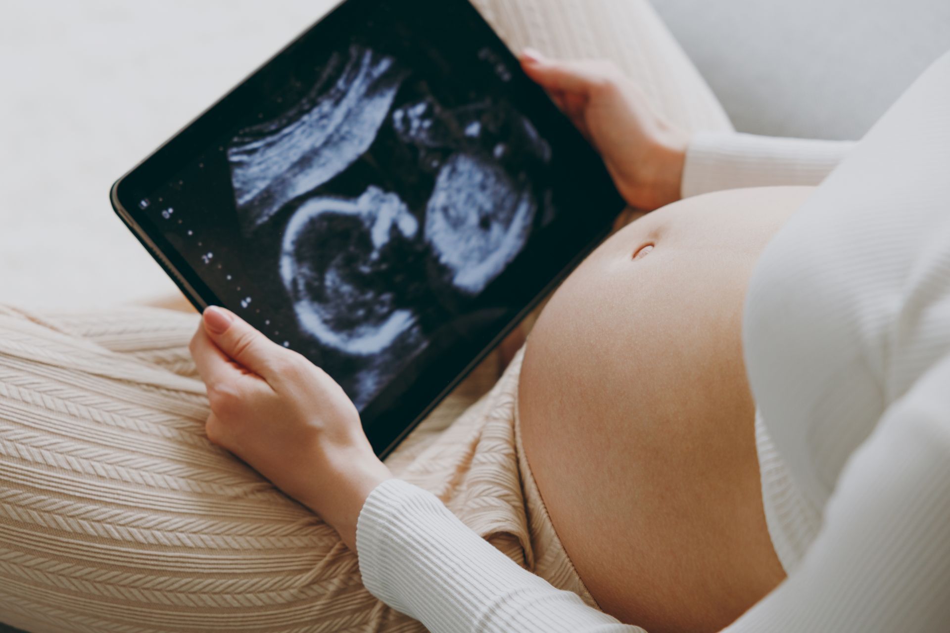 Pregnant person holding a tablet displaying a fetal ultrasound.