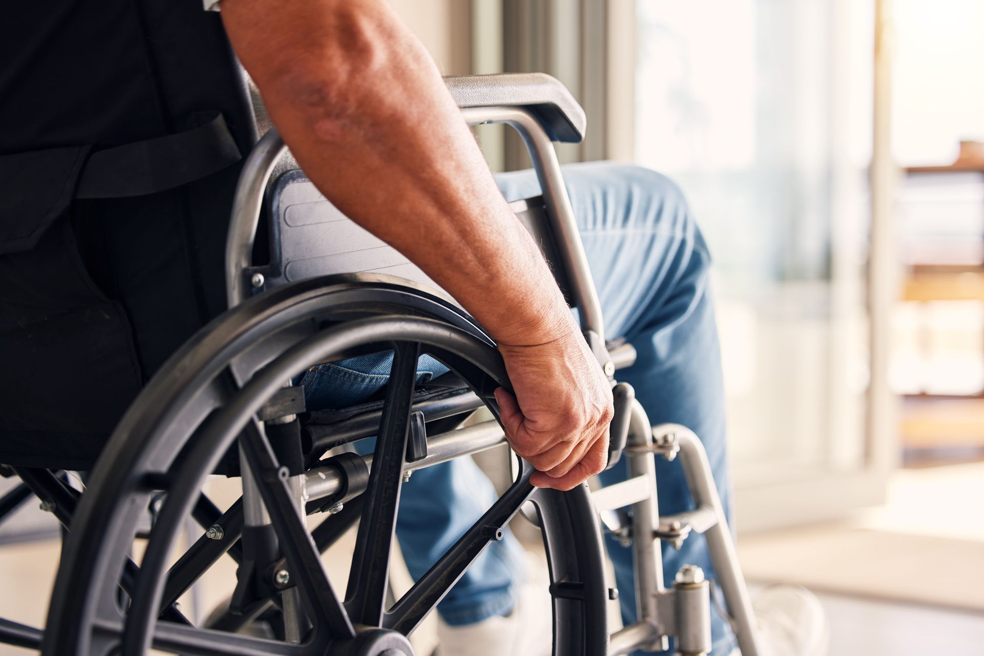 Person's hand on the wheel of a wheelchair, indoors near a doorway.