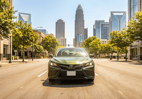 Front-facing view of a Toyota sedan driving through a modern downtown city with a skyline