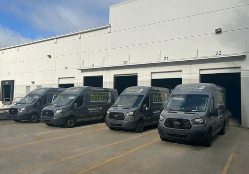 Four dark delivery vans parked outside a white warehouse loading dock.