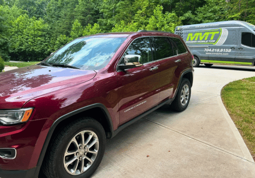 Maroon SUV parked in a driveway beside a utility trailer, with trees in the background