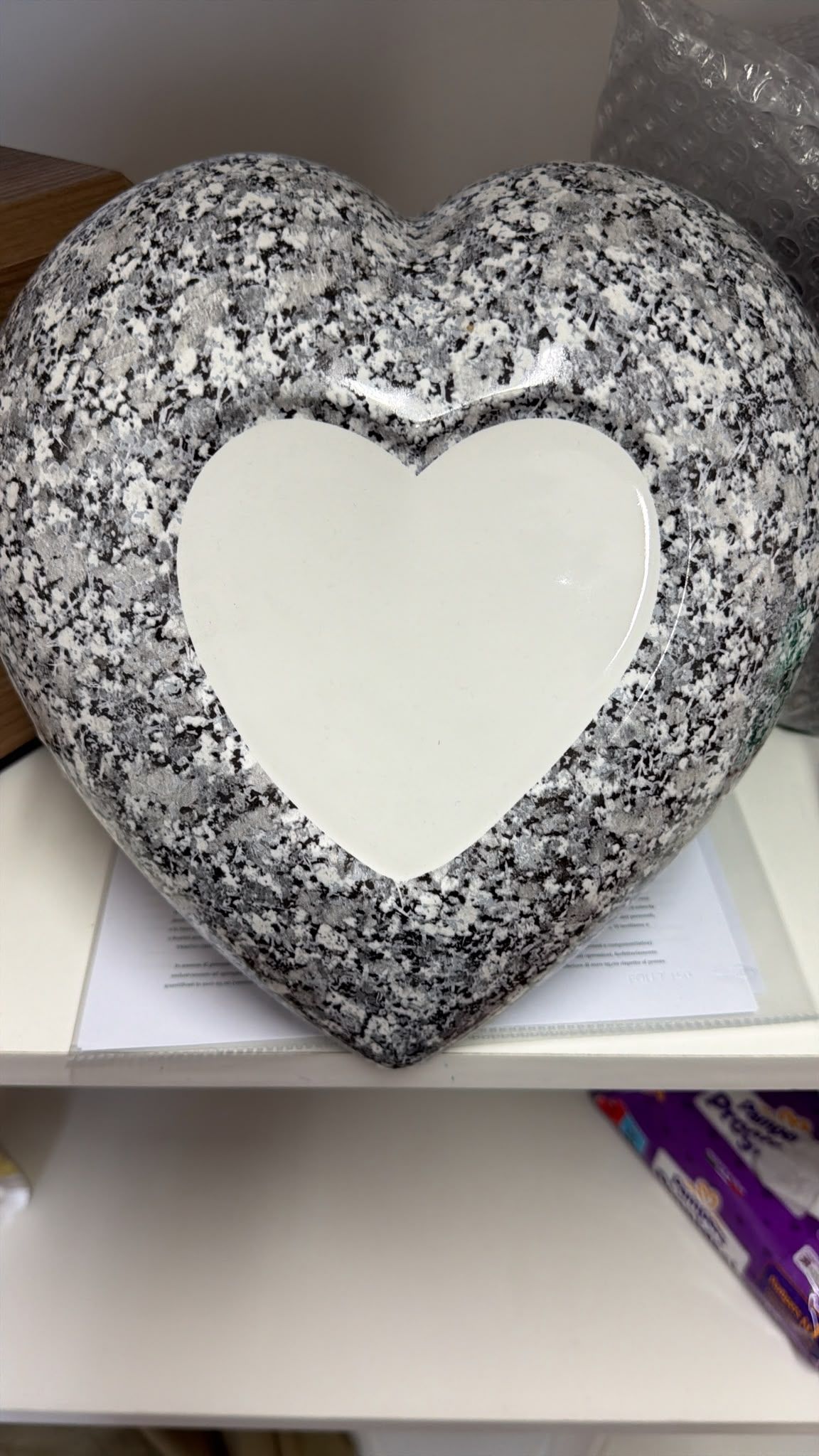 Decorazione argentata a forma di cuore con brillantini e un centro bianco, su una mensola.